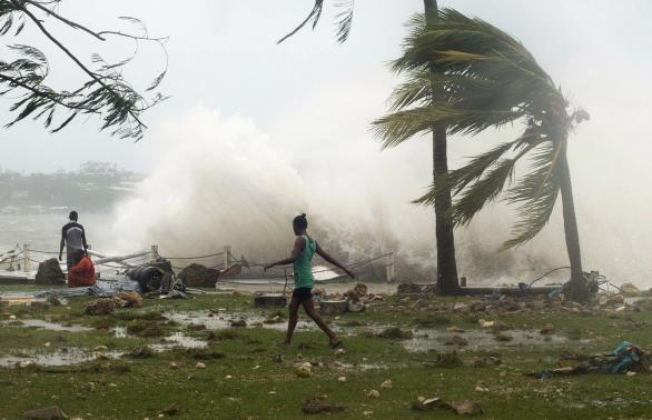 Local residents walk past debris as a wave breaks nearby in Port Vila, the capital city of the Pacific island nation of Vanuatu